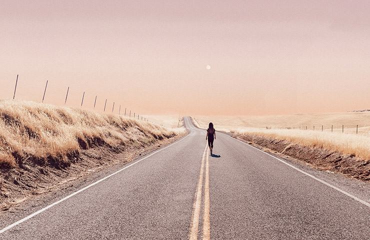 ピンクの空と砂漠脇を歩く女性