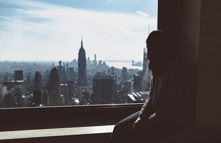 暗い部屋からニューヨークの景色を見つめている女性
