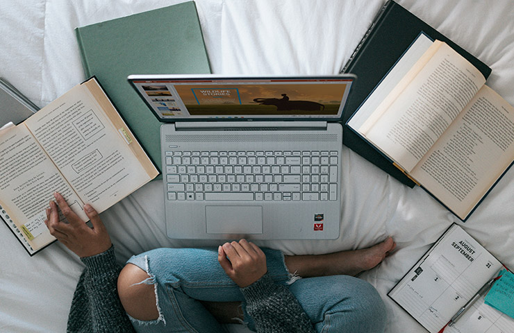 教科書とコンピューターでオンライン学習をしている大学生